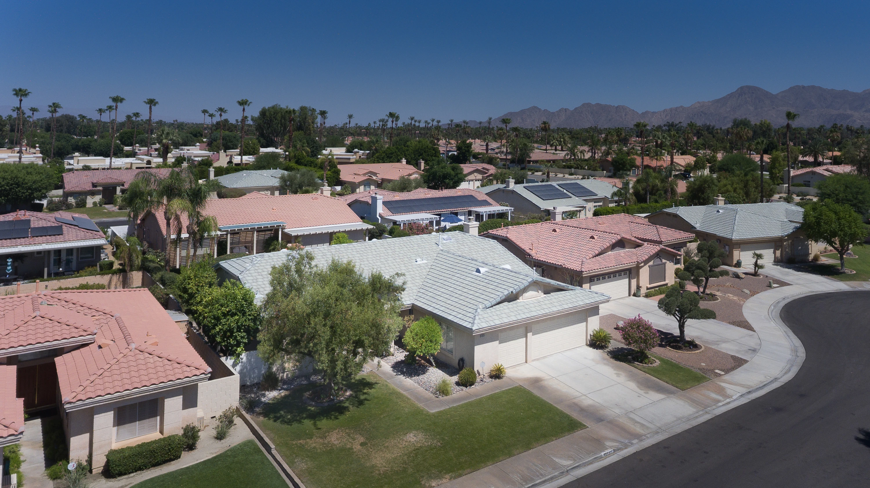 Aerial view of a single-story desert home on a curved street against mountains