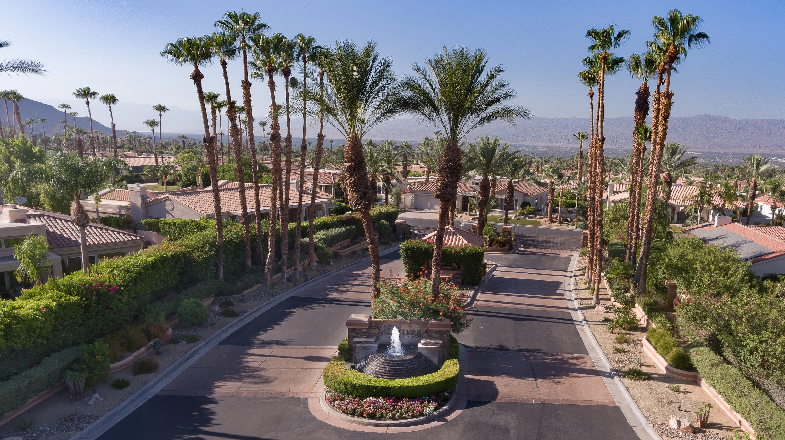 Aerial view of a gated community entrance with a fountain and palm-lined drive